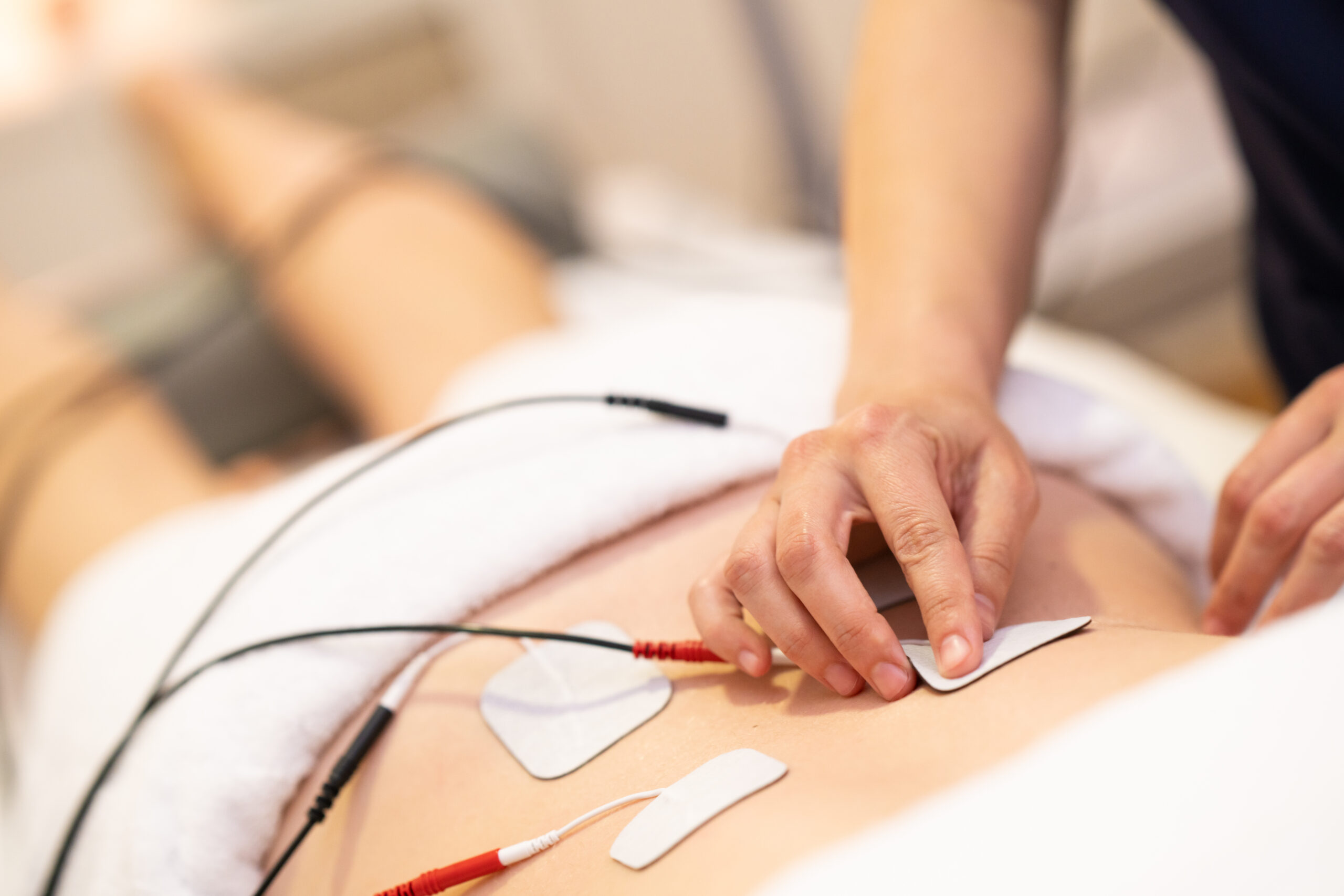 Therapeutin befestigt Elektroden am Rücken einer Patientin