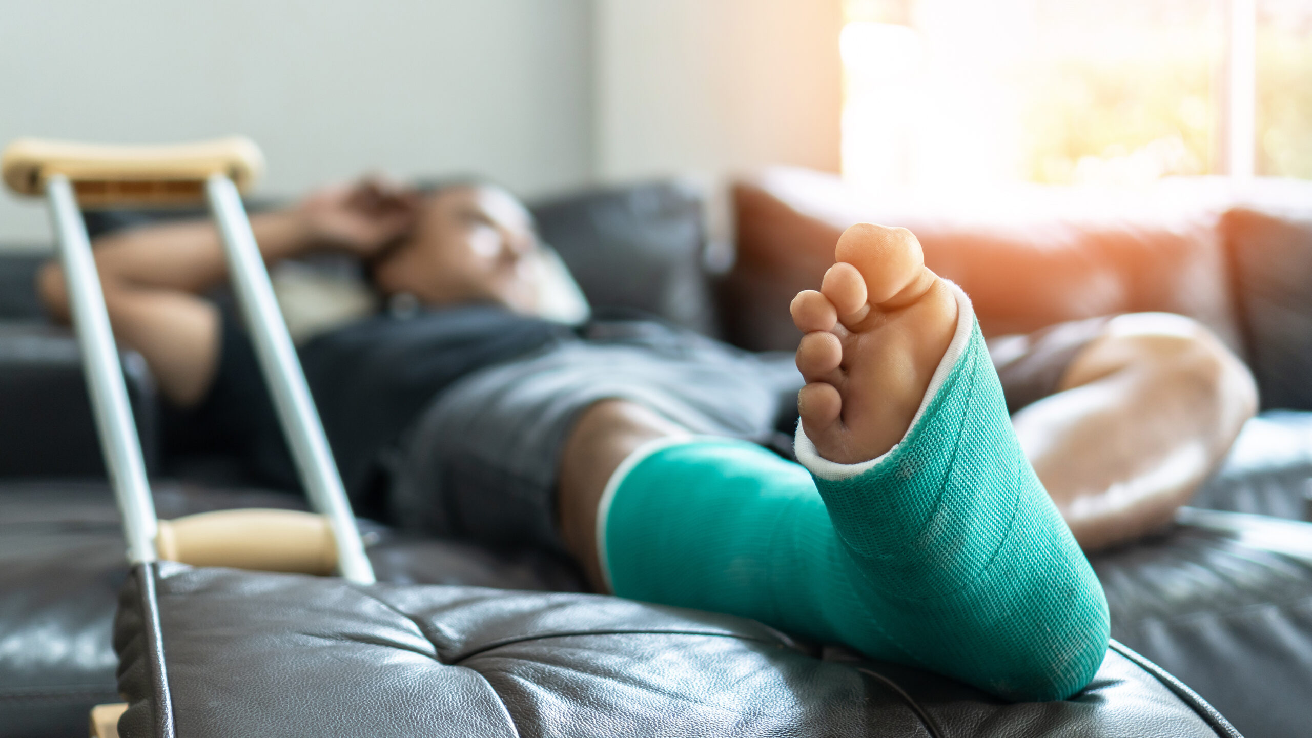 Patient liegt mit Gips am Bein auf dem Sofa
